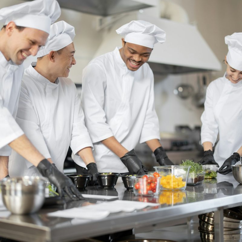 Multiracial team of cooks mixing ingredients for take away food in professional kitchen